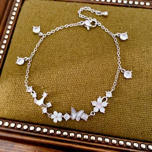 Detailed view of zircon-studded crown and shell butterfly charms on a silver bracelet.