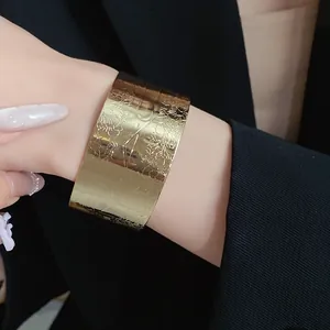 Detailed close-up view of wide gold cuff bracelet featuring vintage engraved floral pattern