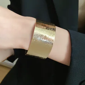 Detailed view of a wide gold cuff bracelet with floral engraving worn on wrist