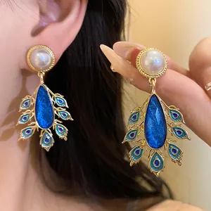 Close-up of elegant vintage gold earrings with white pearls and blue peacock droplets
