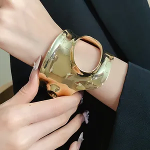 Detail view of a luxury irregular pleated gold cuff bracelet styled with a black blazer.