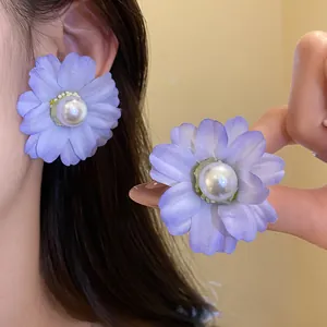 Elegant purple fabric flower stud earrings with center pearl detail shown on model