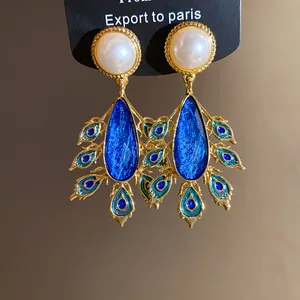 Detailed macro view of vintage gold earrings with pearls and blue peacock waterdrop pendants