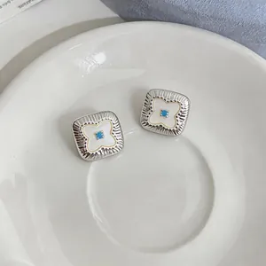Dettaglio di orecchini a lobo quadrati argentati con fiore in conchiglia e perla turchese al centro.