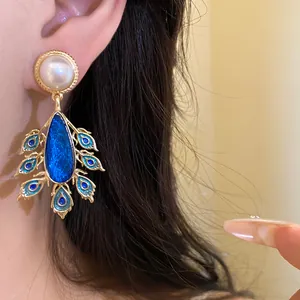 Close-up of vintage gold earring with pearl and blue peacock teardrop pendant details.
