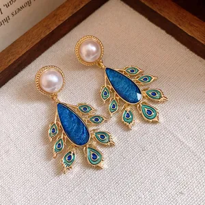 Close-up detail of vintage pearl drop earrings with an ornate blue peacock feather design