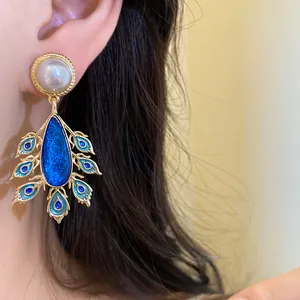 Close-up of vintage gold-tone pearl earring with blue peacock feather pendant