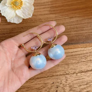 Gros plan de boucles d'oreilles dorées avec perles bleues irisées et pierres violettes.