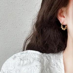 Close-up detail view of minimalist gold beaded hoop earrings worn on ear by Asian model