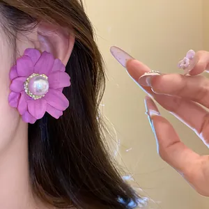 Detail view of a purple fabric flower earring featuring a central pearl on a model's ear