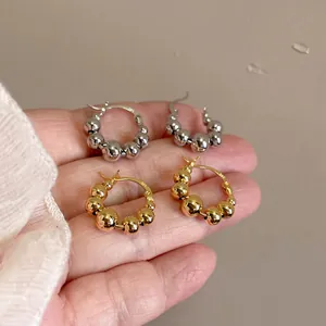 Close-up of gold and silver beaded hoop earrings held in hand to show scale and detail