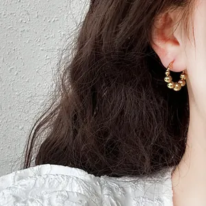 Close-up detail of a minimalist gold beaded hoop earring worn on a model's ear
