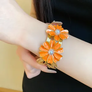 Close-up of elegant orange enamel flower and pearl double-layer open cuff bracelet for women