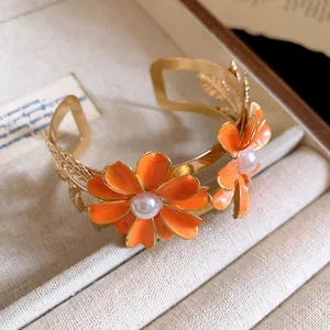 Close-up of golden double-layer cuff bracelet with orange enamel flowers and pearls