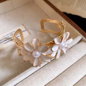 Detailed view of an elegant gold cuff bracelet with white enamel daisy flowers and pearls.