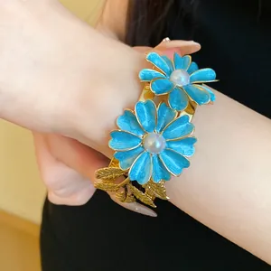 Close-up of blue enamel flower bangle with pearl center and gold leaf detail.