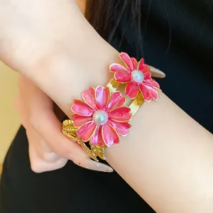 Detail view of a double-layer gold cuff bracelet with pink enamel flowers and pearls
