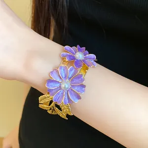 Elegant gold cuff bracelet with purple enamel flowers and pearls on a woman's wrist