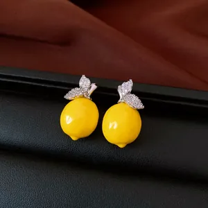 Macro detail of vibrant resin lemon earrings featuring sparkling zircon-encrusted leaves