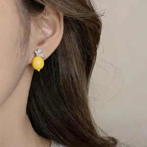 Detailed close-up view of a yellow resin lemon stud earring worn on a model's ear