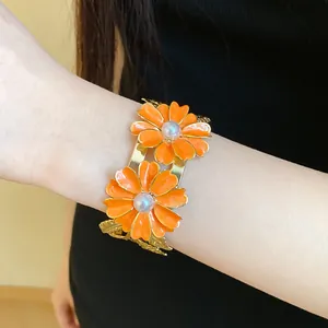 Close-up of orange enamel flower bangle with pearls on gold-tone double-layer band.