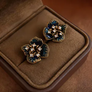 Macro view of dark blue enamel flower stud earrings with rhinestones in a brown velvet box