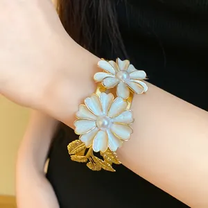 Detail view of golden open bangle featuring elegant white pearl flower motifs on wrist
