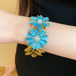 Detail of elegant gold-toned open bangle featuring blue enamel flowers and pearls