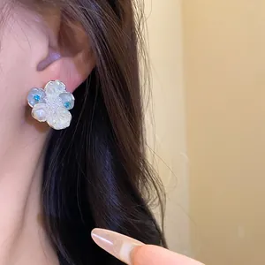 Close-up of elegant floral stud earring with pearls and blue zircons worn by a model