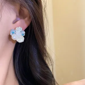 Detailed close-up of exquisite pearl flower stud earring with blue zircon on model ear
