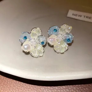 Detail view of exquisite pearl and blue zircon flower stud earrings on a beige tray