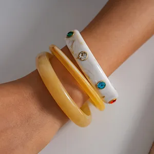 Dettaglio di tre bracciali in resina marmorizzata con strass colorati sul polso