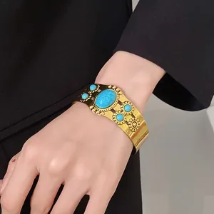 Close-up of vintage gold cuff bracelet with turquoise stones on a wrist.