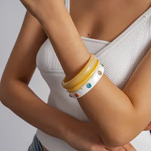 Dettaglio di tre bracciali in resina marmorizzata con strass colorati indossati da una modella.