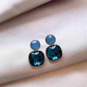 Elegant close-up of vintage square blue crystal stud earrings on champagne satin backdrop.