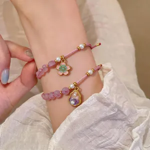 Close-up of handmade braided bracelet with pearl and enamel flower charms