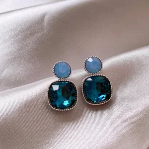 Close-up detail of vintage square stud earrings with faceted deep blue crystals on satin