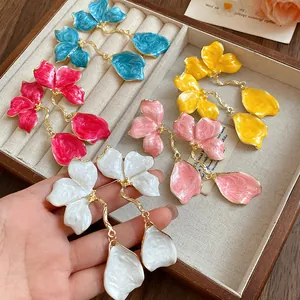 Detail view of retro enamel flower drop earrings in multiple colors held in hand