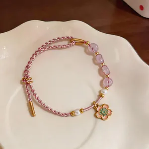 Detailed macro shot of hand-woven pink cord bracelet featuring pearls and cherry blossom charm