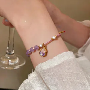 Close-up of a hand-woven purple beaded bracelet with pearl and flower charm on wrist