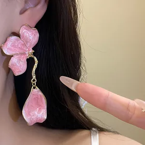 Close-up of elegant pink enamel flower drop earrings worn on ear with golden finish.
