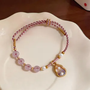 Close-up of handmade braided rope bracelet with pearls and gourd charm.