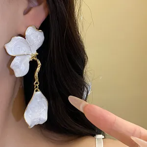 Detailed close-up showing the texture of white enamel flower drop earrings with gold trim