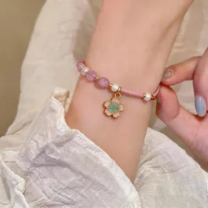 Close-up of hand-woven pink cord bracelet featuring pearls and cherry blossom charm