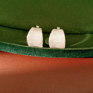 Detailweergave van minimalistische zilverkleurige oorringen met een geborstelde afwerking