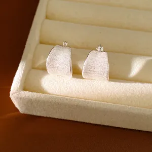Close-up van minimalistische oorbellen met een fijn geborstelde zilveren metalen textuur