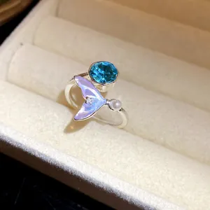 Vue macro de la queue de sirène irisée et du zircon bleu sur une bague ouverte en argent
