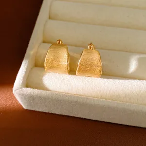 Detailweergave van 18k vergulde oorbellen met geborstelde textuur in een fluwelen tray