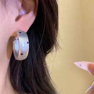 Elegant minimalist matte silver hoop earrings with black polka dots on model's ear