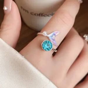Gros plan d'une bague argentée ouverte avec cristal bleu et queue de sirène holographique.